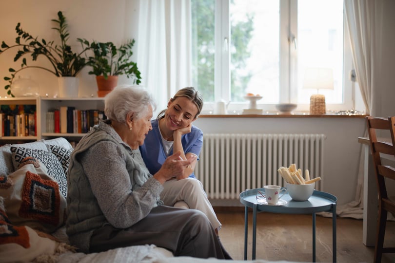 Caring healthcare worker visiting a senior patient at home, talking with her in the living room