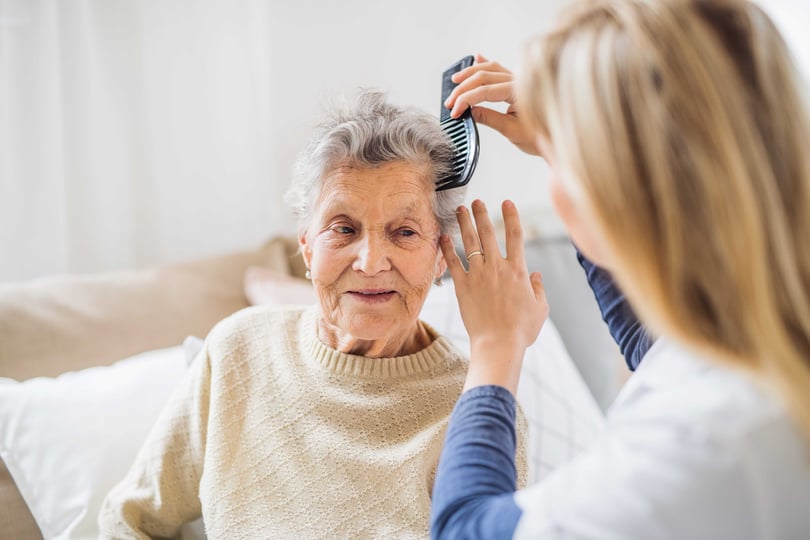  A health visitor combing hair of senior woman at home