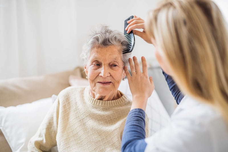  A health visitor combing hair of senior woman at home