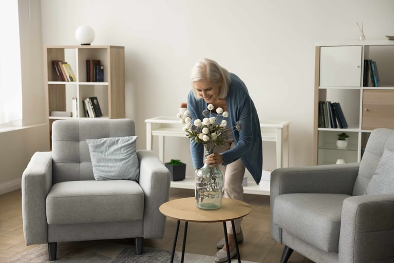 Happy blonde retired mature woman decorating home living room interior