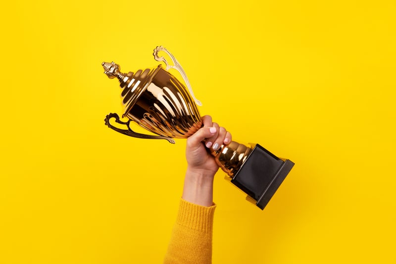 A hand holding a trophy in the air with a yellow background 