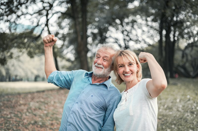 A happy senior couple flexing their biceps in the park.