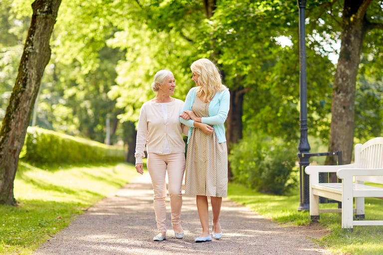 A senior woman walking in the park with her daughter. Their arms are linked.