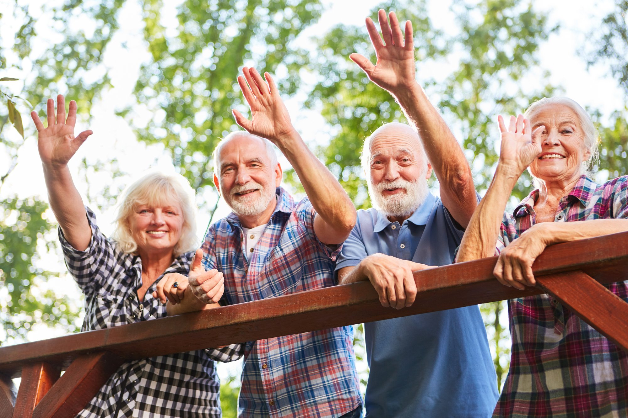 Four seniors smiling and waving at the camera while standing on a balcony