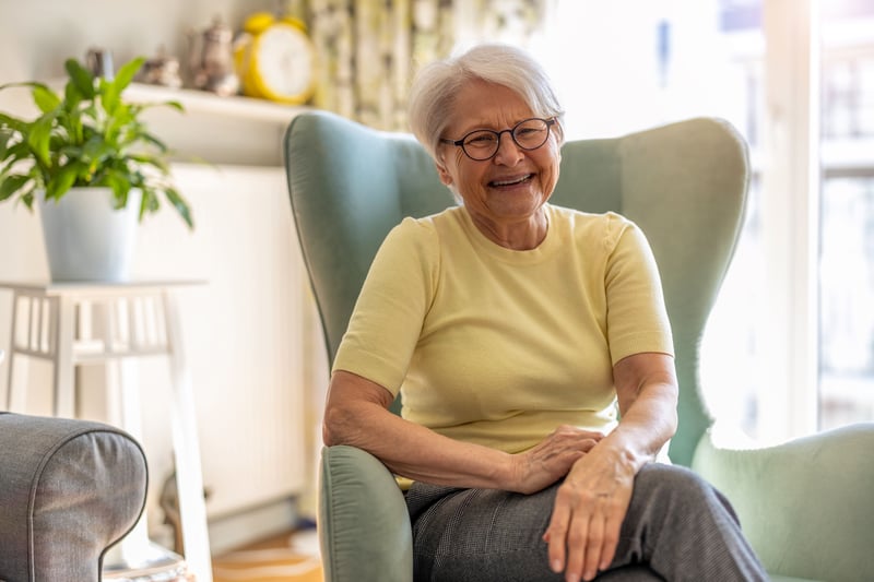 A smiling senior woman sitting in a chair in a well-lit room. 