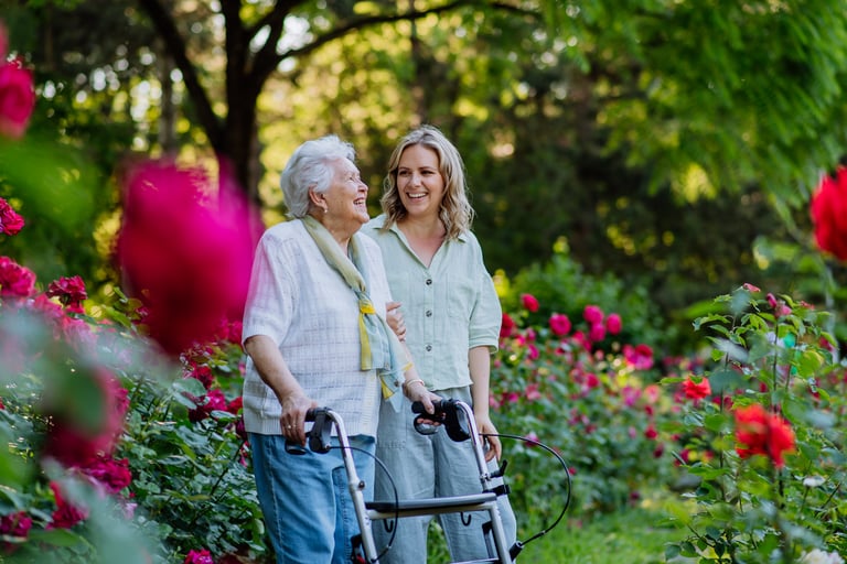 Adult granddaughter supporting her senior grandmother when taking her for walk with walker in park in summer.