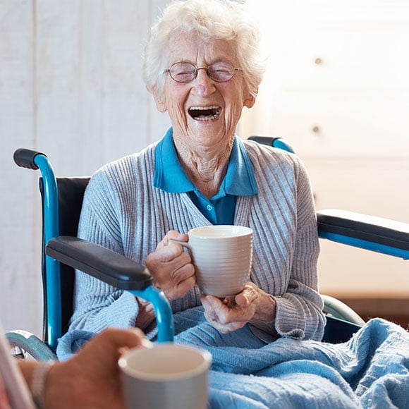 An older woman laughing while holding a cup of coffee. 