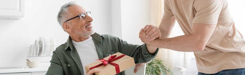 Smiling man holding gift box and shaking hands with son