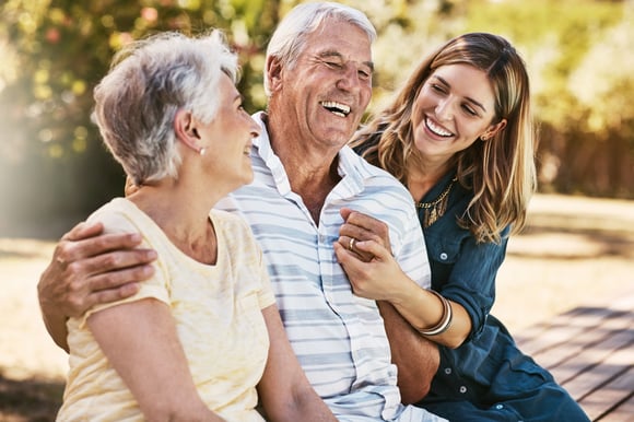 Two older adults laughing and spending time with a younger woman. 