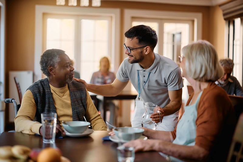 A happy senior man and woman talking to a caregiver in a dining room at senior living community.