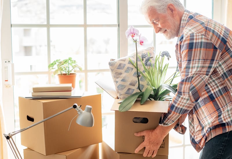 An older man happily moving boxes around his house.