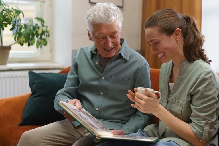An older man and his granddaughter smiling while looking at a family photo album.