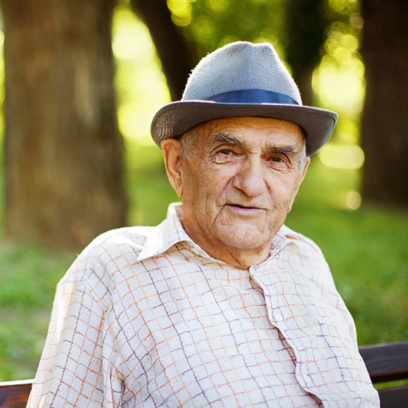 An older man in a park smiling at the camera.
