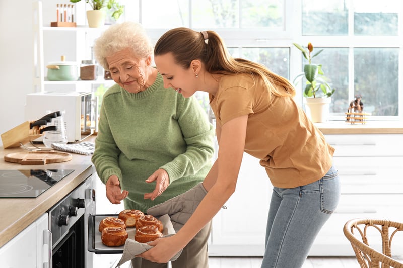 A senior woman with her granddaughter taking cinnamon buns out of the oven.