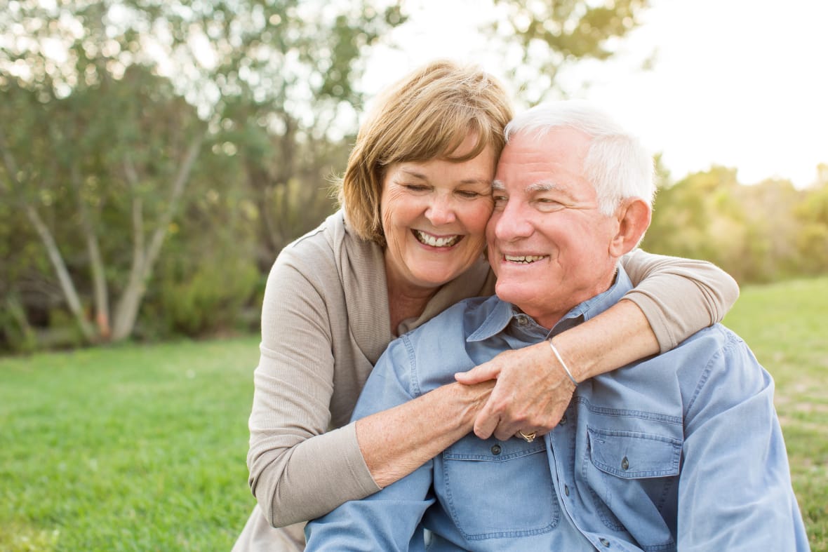 A woman hugging a senior man and smiling.