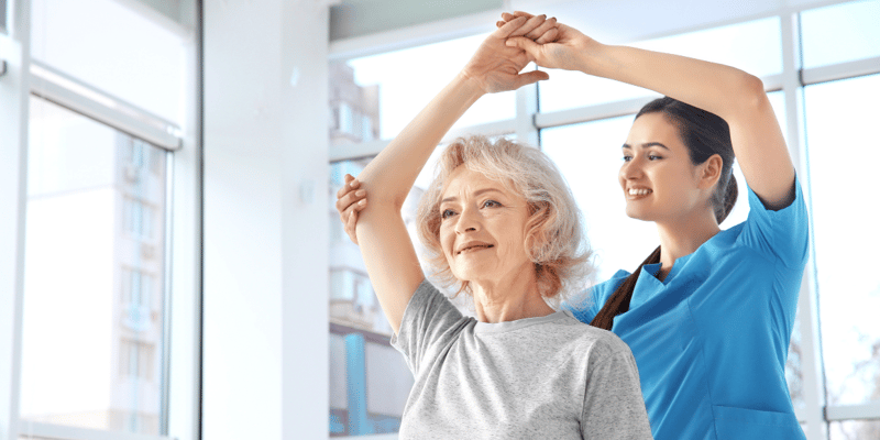An older adult stretching with her short-term rehab caregiver.
