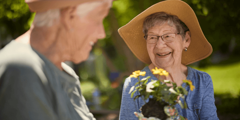 An older woman smiling and holding a plant out toward her friend