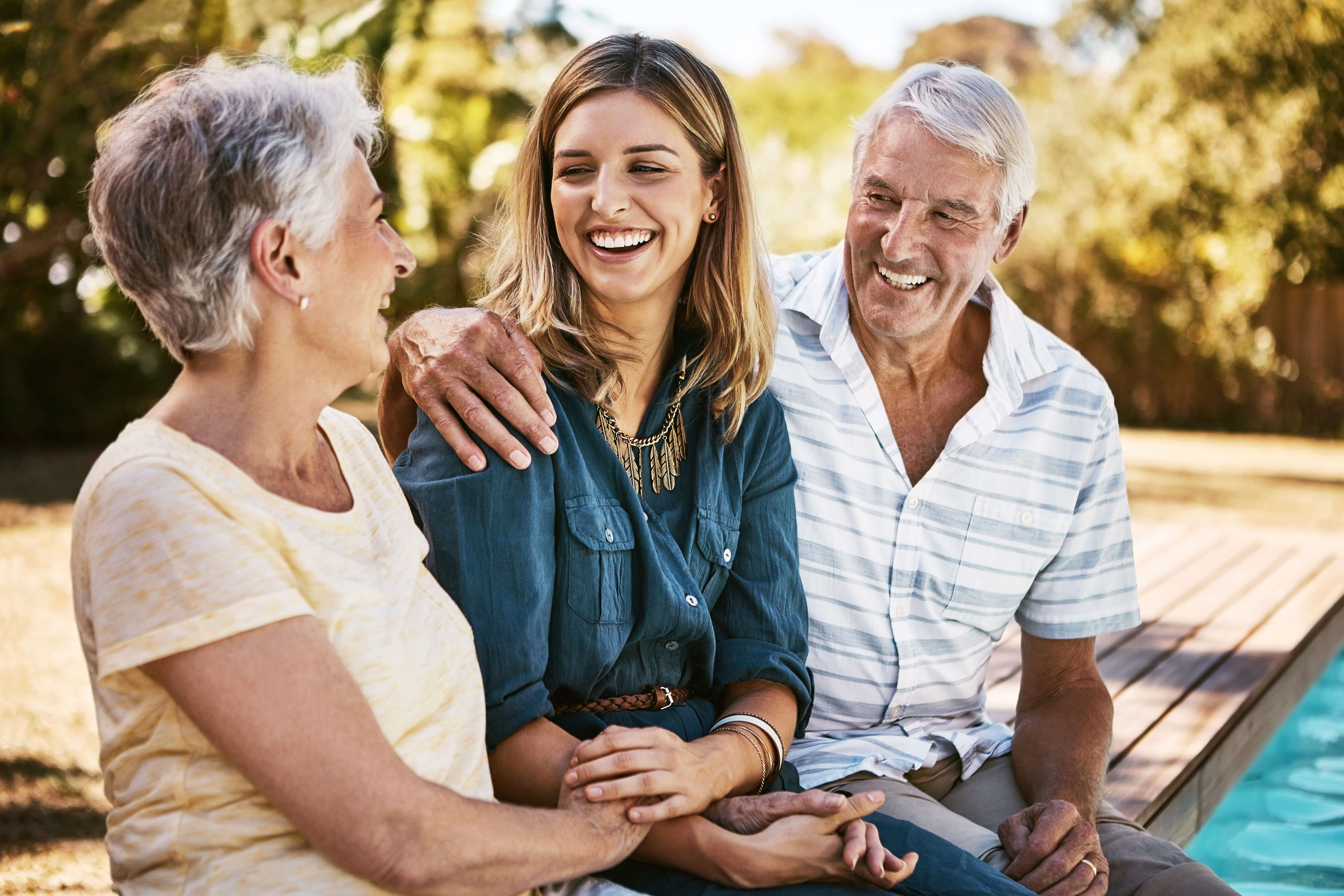 Two older adults and a young woman embracing by the pool