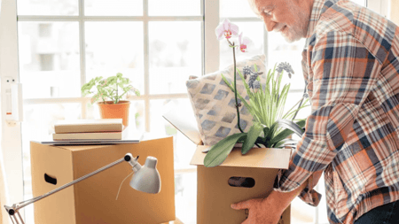 An older man happily moving boxes around his house.