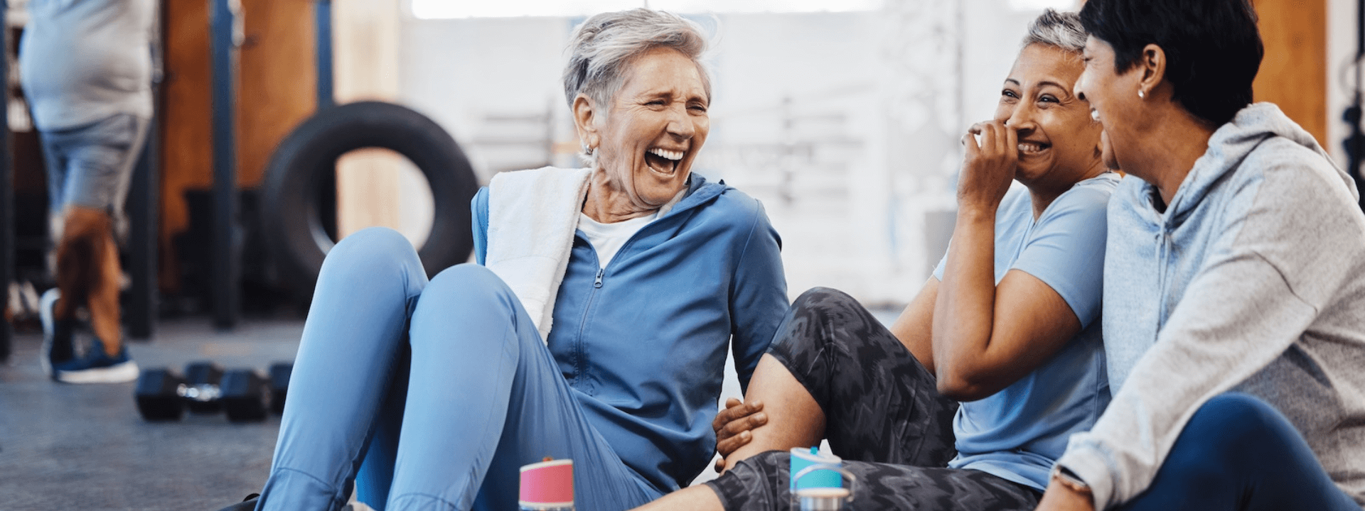 Three people sitting and laughing in a gym setting.