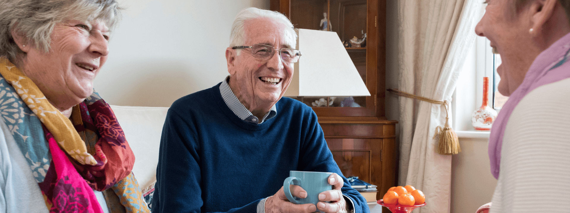 Three elderly people sitting in a living room, laughing and chatting.