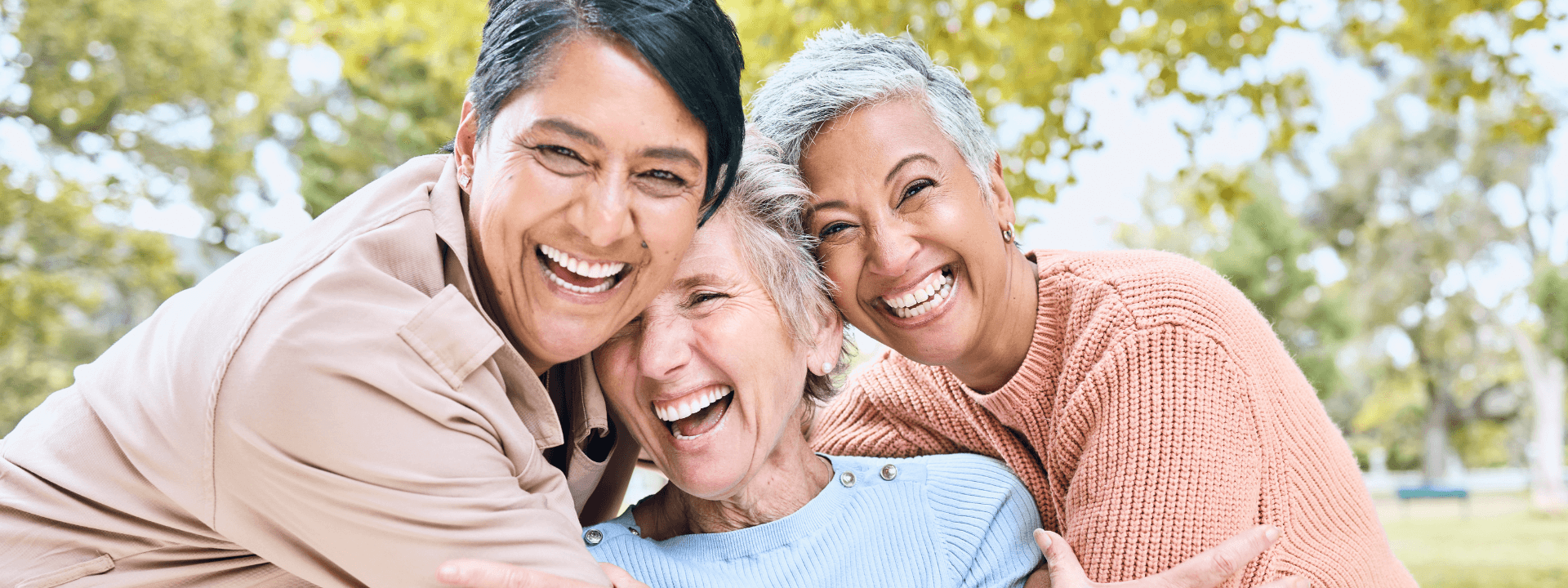 Three people smiling and embracing outdoors.