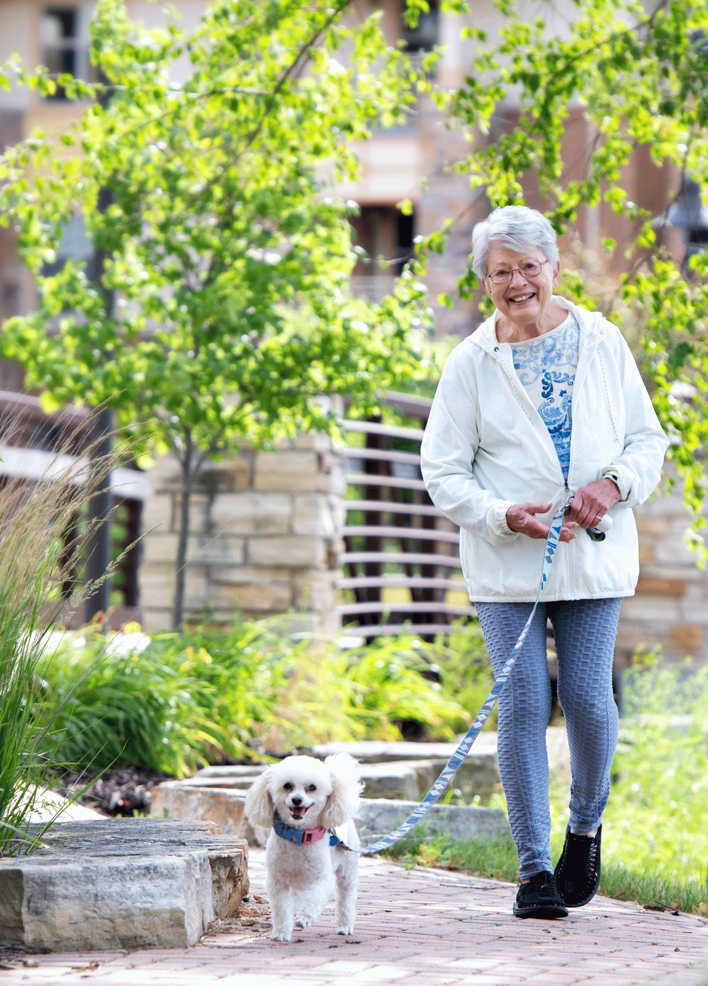 Senior woman outside walking a small white dog on a leash