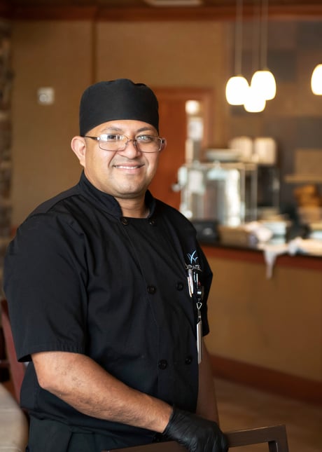 A chef wearing a black uniform while smiling at the camera