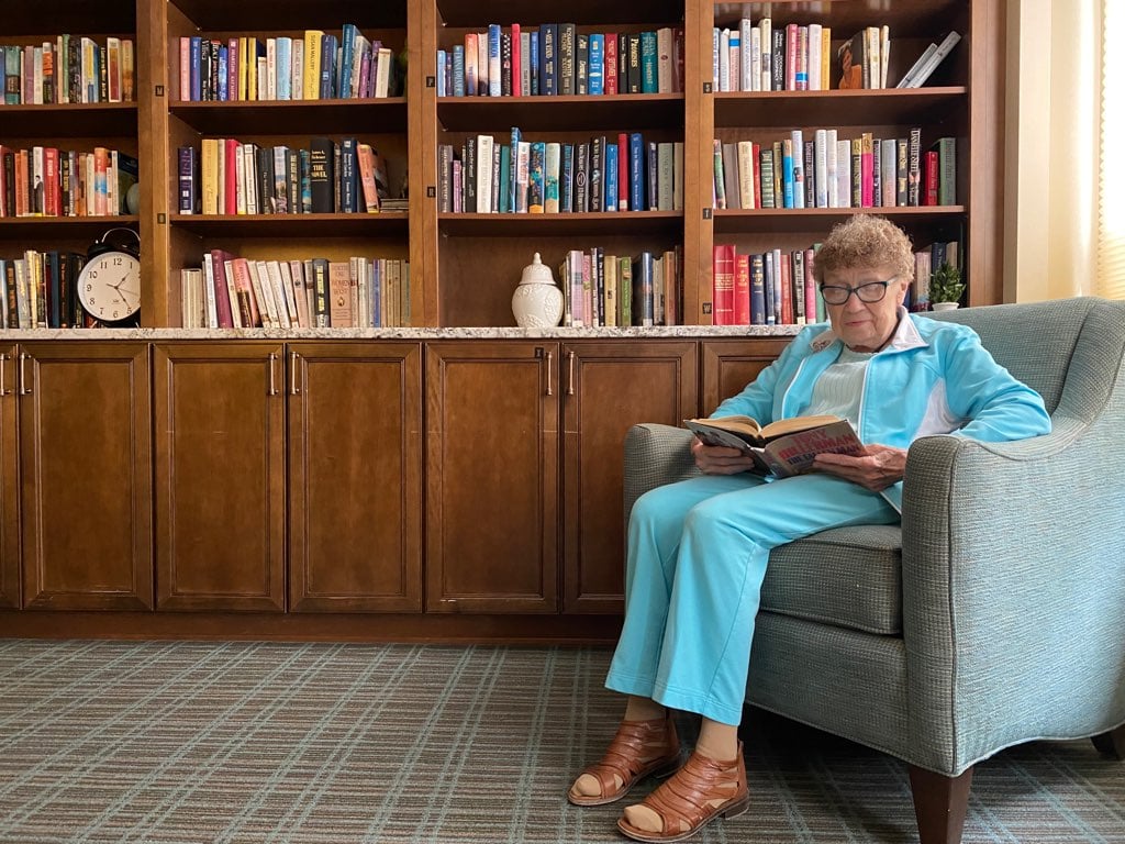 senior woman reading book on chair in library