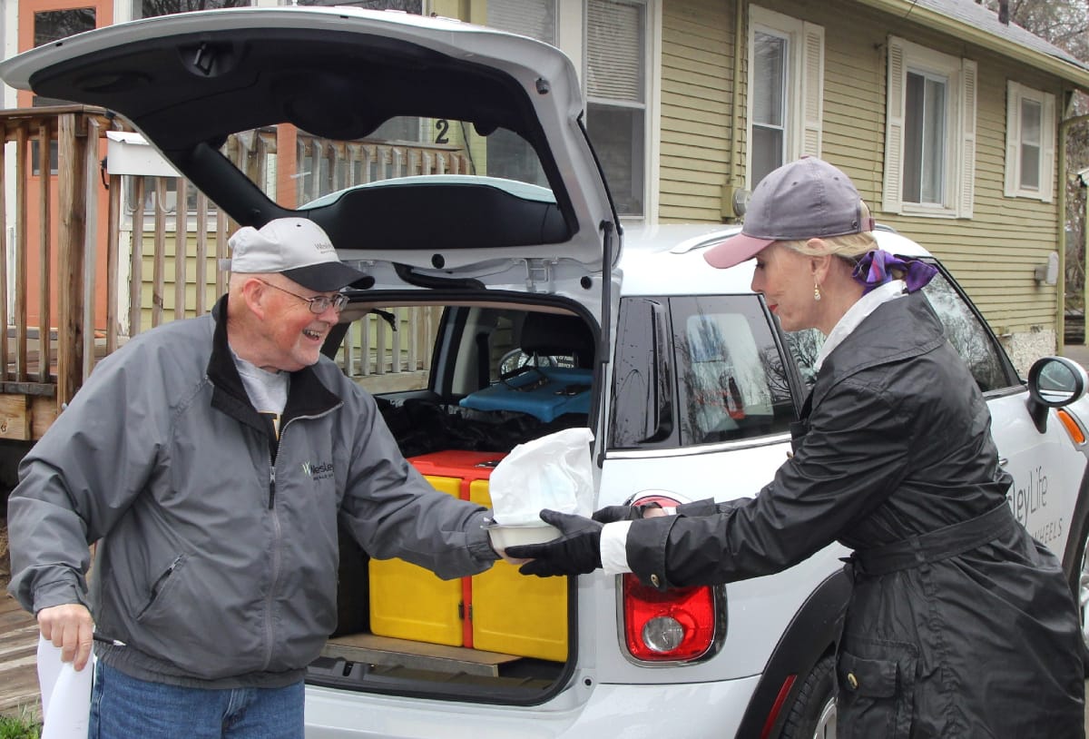 Two people handing off a Meals on Wheels meal
