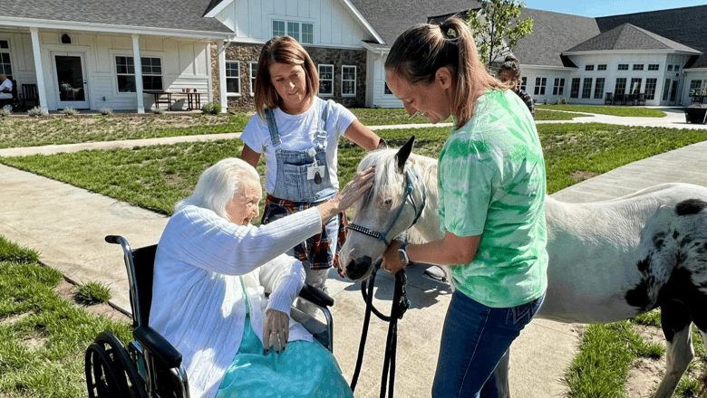 Two team members helping a resident pet a pony