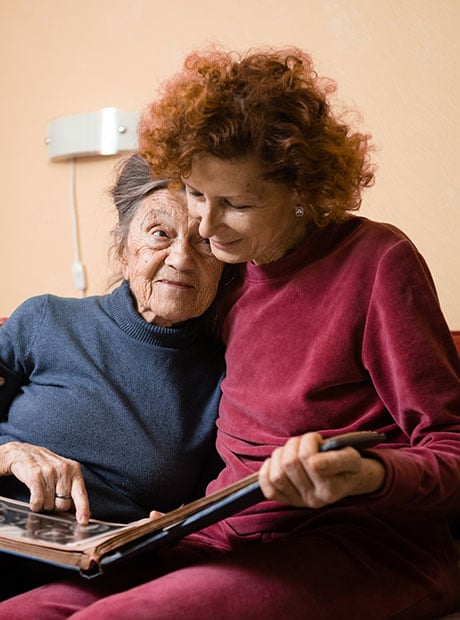 Senior females looking album photos together while sitting on sofa