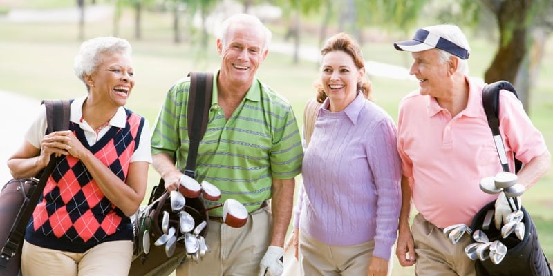 A group of senior friends smiling and having fun on a golf course.