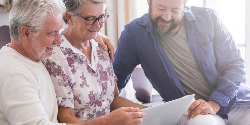 A senior couple and their son looking at levels of living options on a laptop.