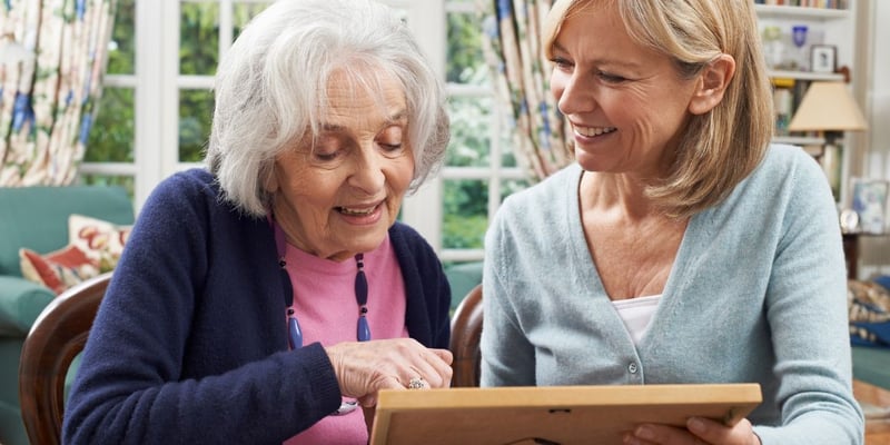 A senior woman and her daughter looking at a framed photo and smiling.