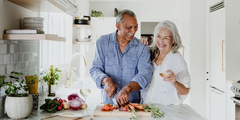 A senior couple chopping vegetables and enjoying each other’s company.