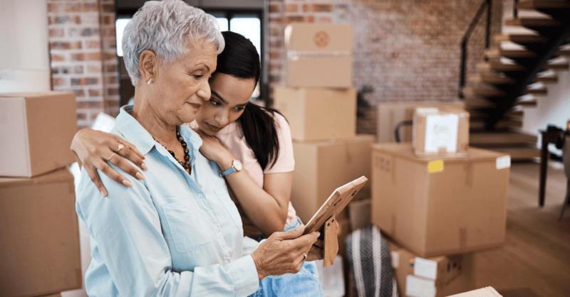 Mother and daughter looking at picture while packing boxes to move to assisted living.