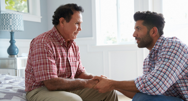 adult son comforting father suffering with dementia