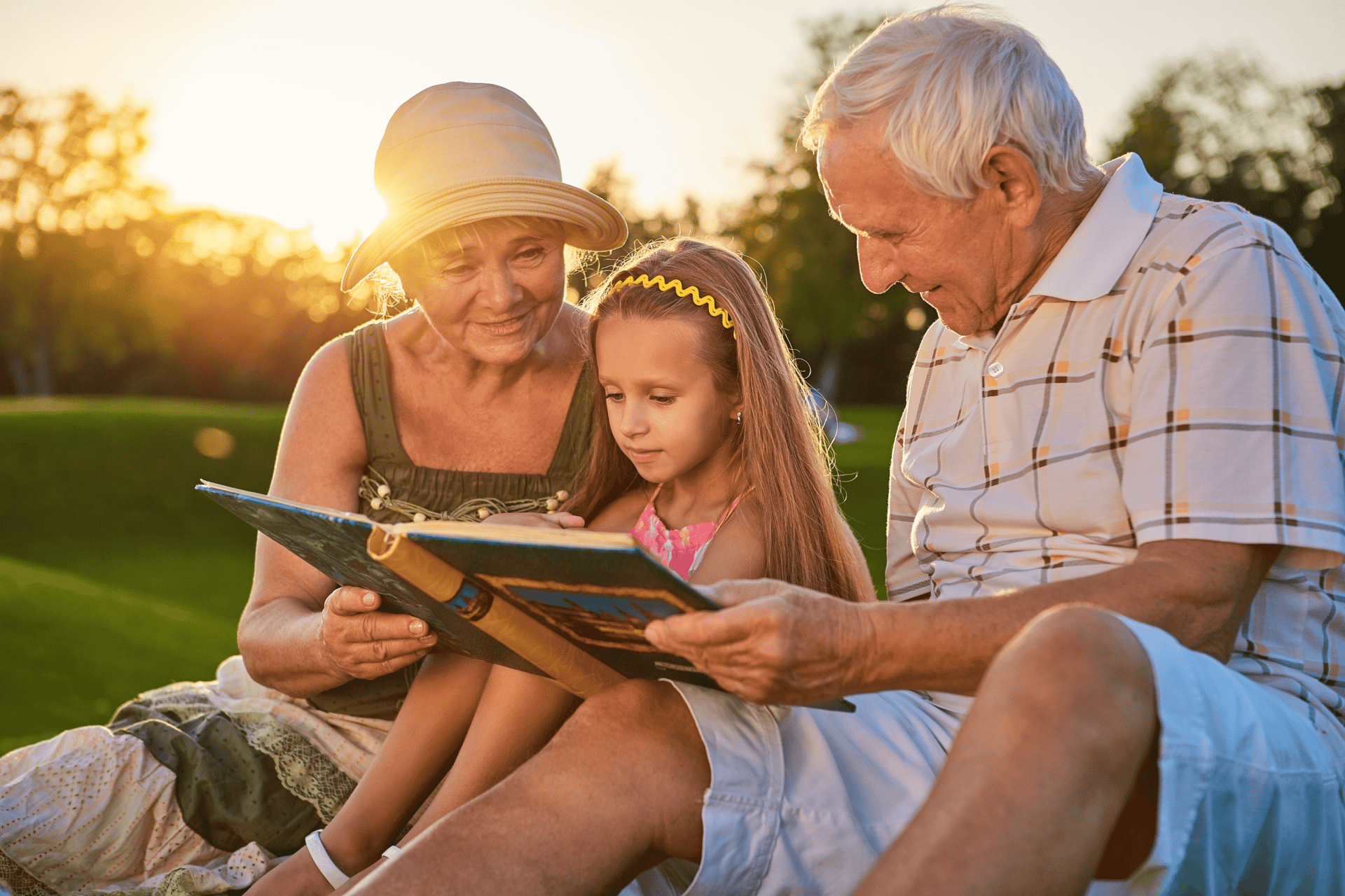 senior grandparents reading a book with their granddaughter