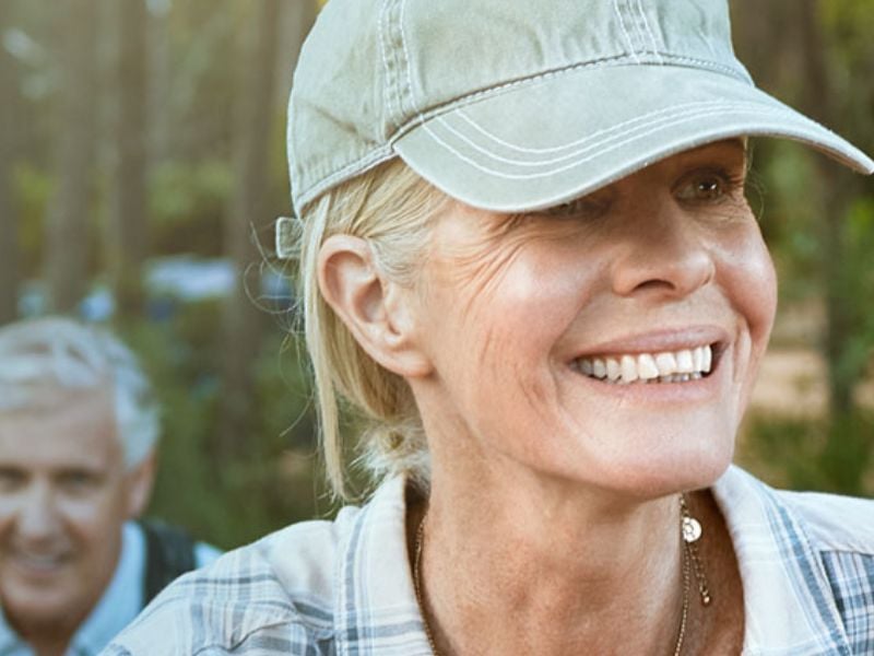 An older woman wearing a baseball cap and smiling. 