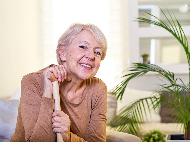 Elder lady sitting on the couch with wooden walking stick and smiling