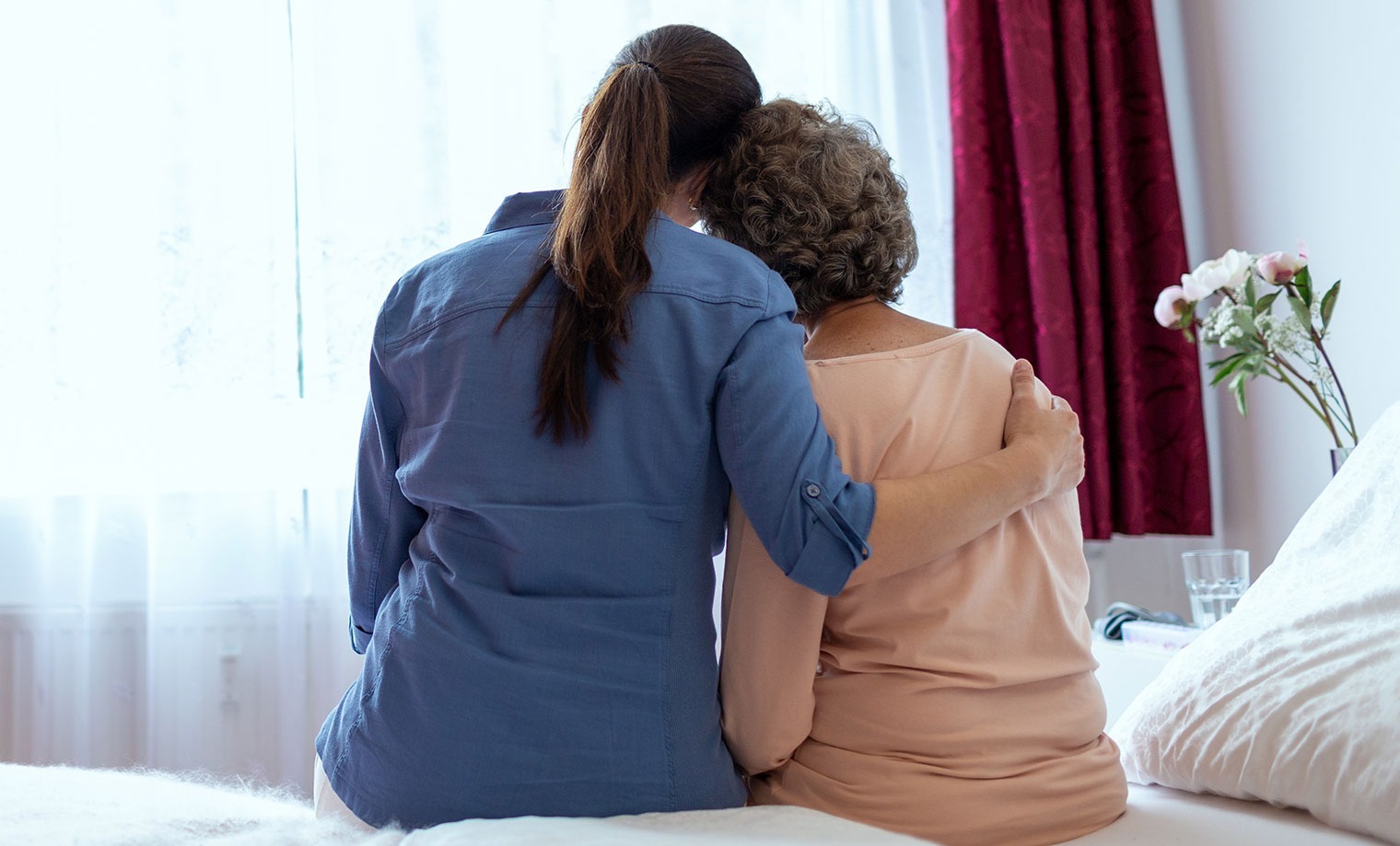 Female Home Nurse Hugging Elderly Woman on Bed