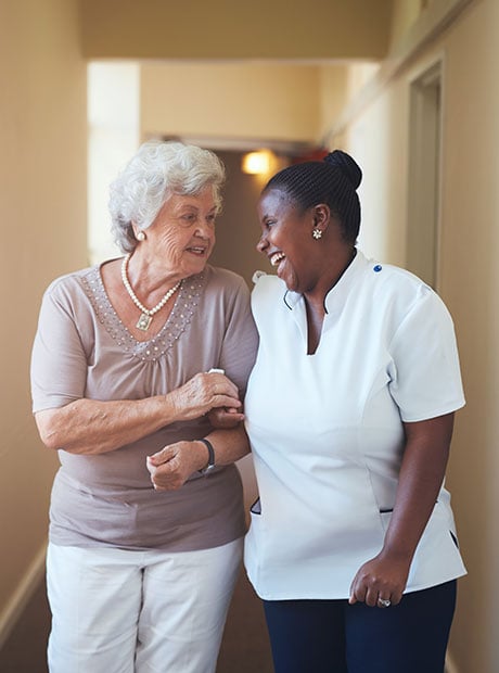 Happy female caregiver and senior woman walking together smiling
