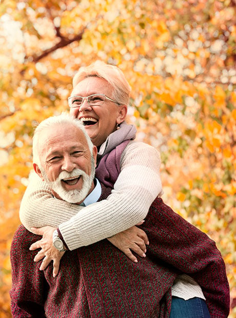 A senior couple embracing in front of fall foliage. 