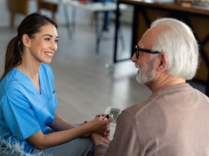 Kind smiling young nurse talking to happy satisfied older senior man in retirement