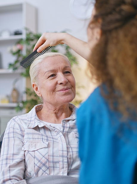 Medical worker combing hair of a senior woman in assisted living facility