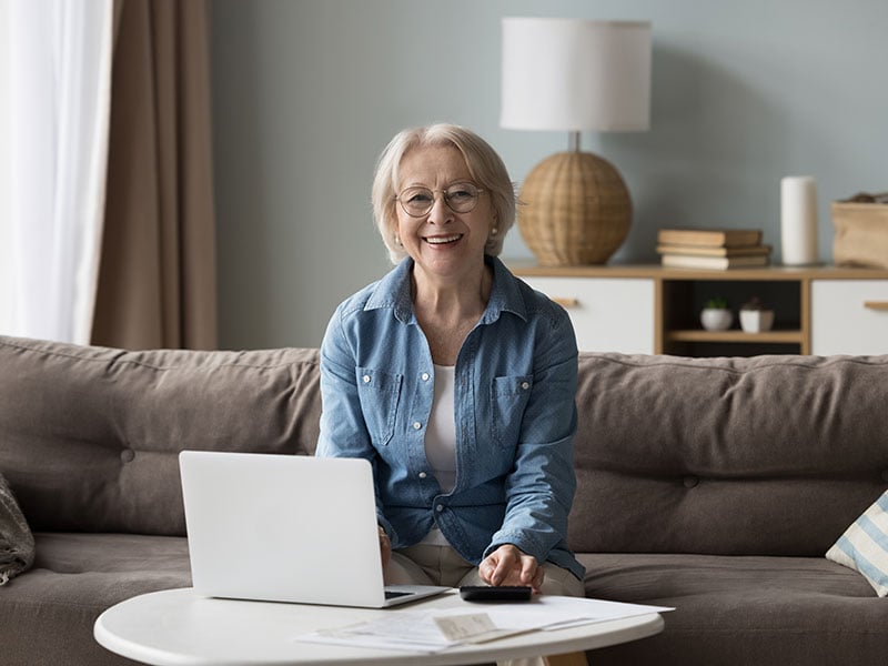 Portrait of happy senior elderly retired woman sit on couch with laptop