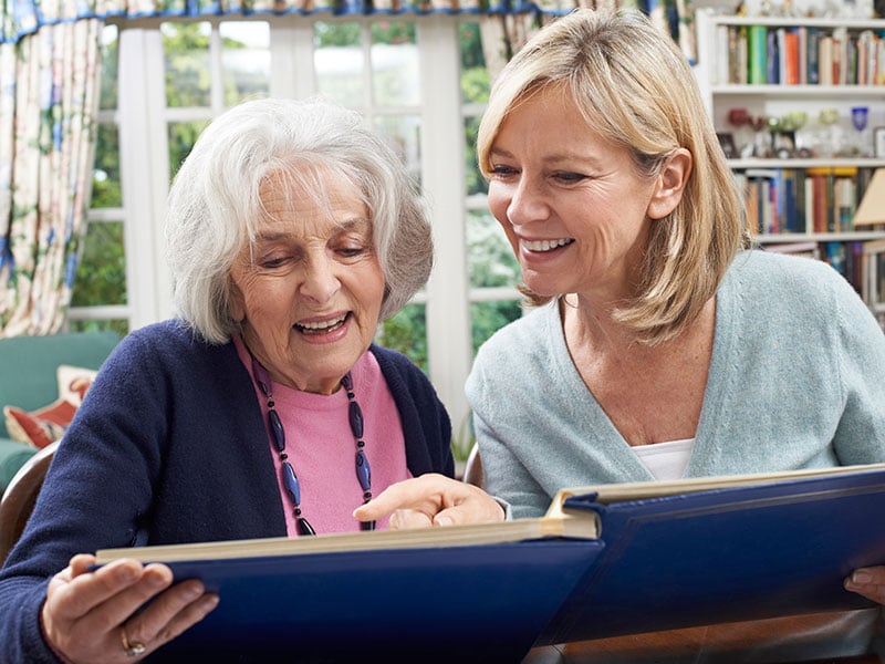 Senior Woman Looks At Photo Album With Mature Female friend