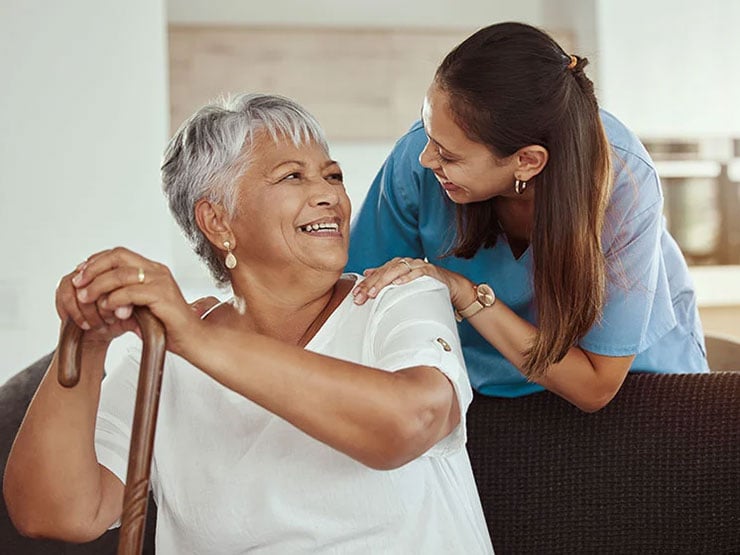 senior woman with caregiver smile while sitting on a livingroom sofa in a nursing home