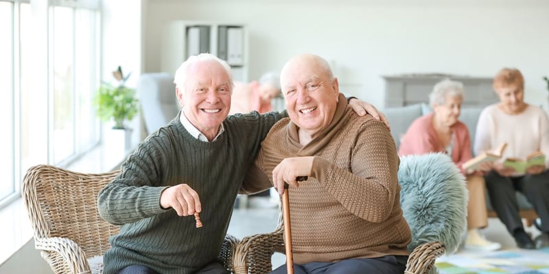 Two smiling men playing chess in a senior living community.